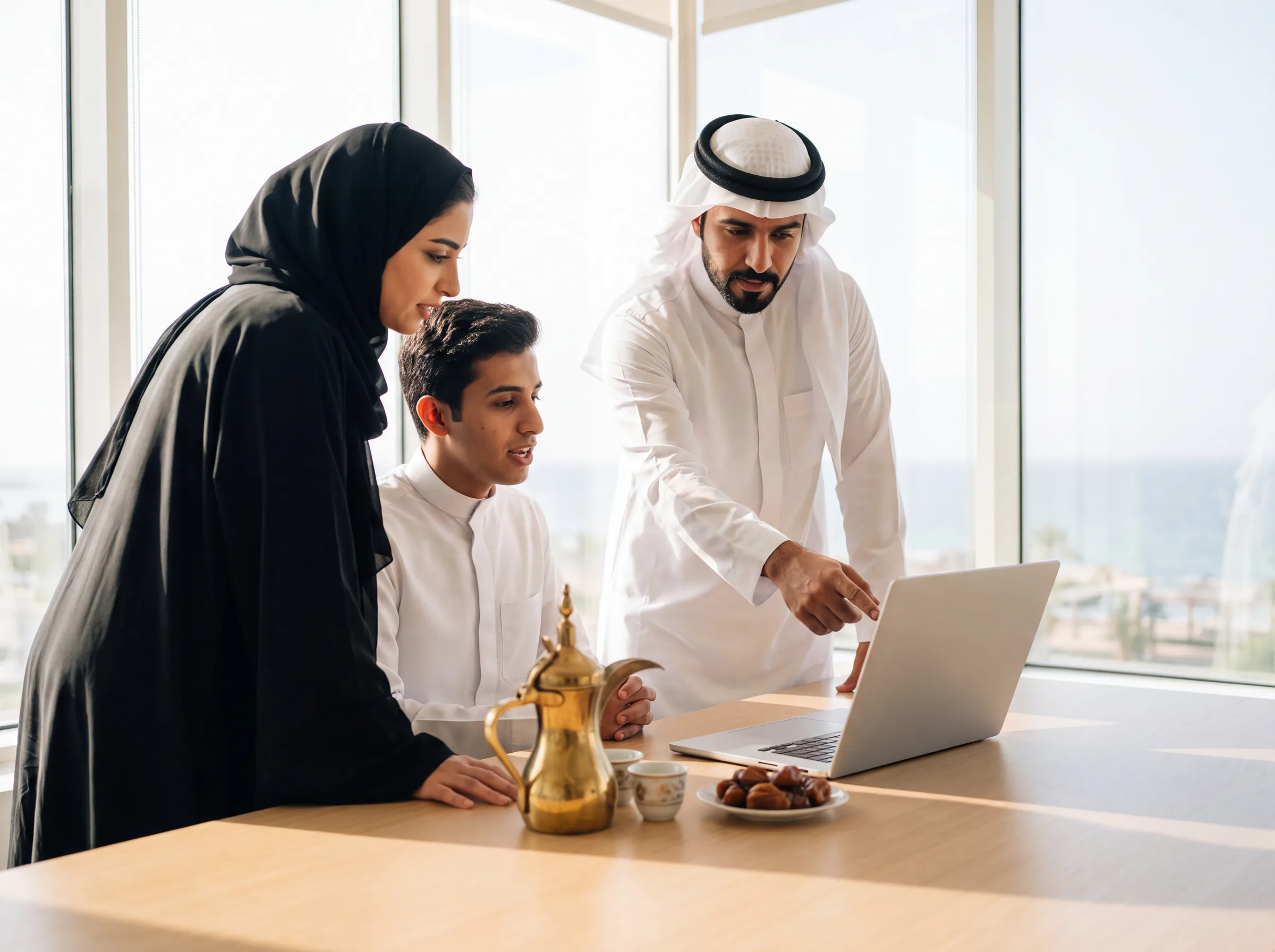 ثلاثة زملاء حول حاسوب محمول على طاولة عليها قهوة عربية وتمر، مع إطلالة على البحر